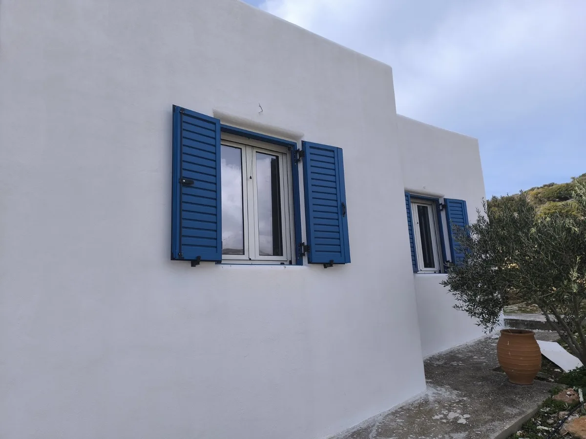 The whitewashed wall of a house with a window and hinged blue shutters, Paros