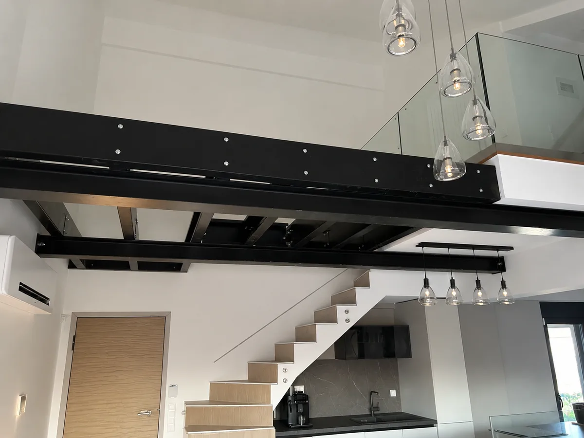 The finished steel mezzanine with a glass railing and stairs, in a house with an open living area